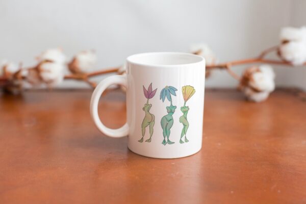 white mug with beautiful illustration of 3 flowers with the bodies of human women.