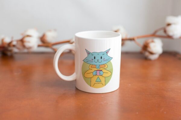 Cat Bud Mug is a plain white mug with an illustration of a cute blue cat sipping on a hot beverage